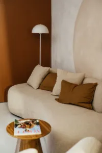 Beżowa kanapa z poduszkami na tle brązowej ściany